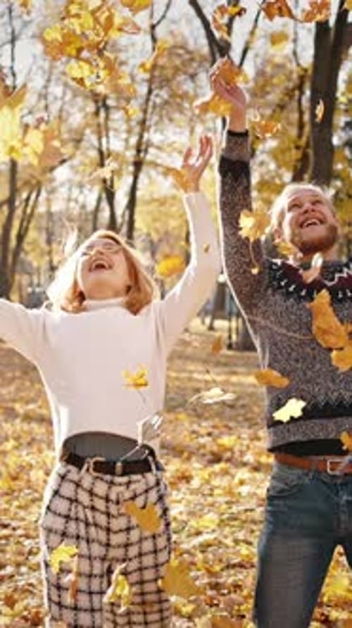 Autumn Fun Young Happy Man and Woman Throwing Bunches of Fallen Leaves in Park and Laughing Under