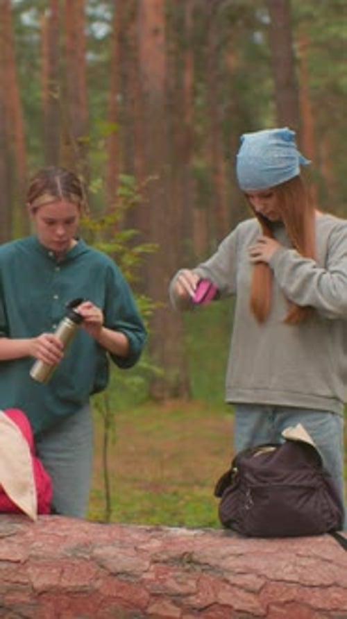 Young Women Take Forest Break with Thermos and Hair Brush