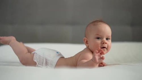 Side View of Sweet Infant Baby Wearing White Diaper Lying on Stomach and Happily Waves Arms and Legs