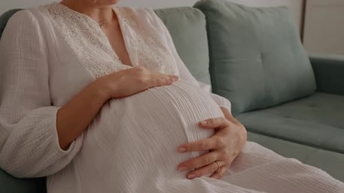 Nahaufnahme einer schwangeren Frau in den frühen Wehen, die plötzliche Kontraktionen spürt, wenn sie auf dem Sofa sitzt.