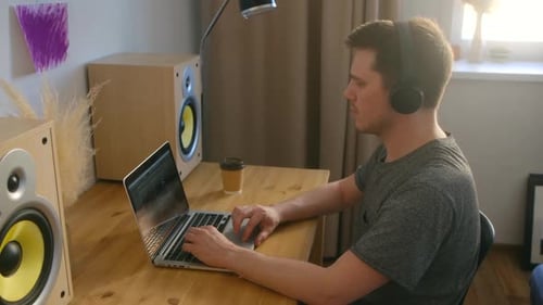 Young Man Using Laptop at Desk with Speakers