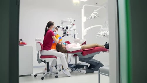 Female dentist with assistant treats teeth using a microscope in a modern dental clinic. Closeup