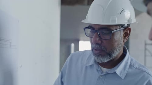 Architect Marking Floor Plan and Talking to Colleague at Construction Site