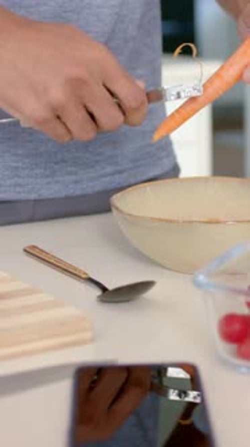 Vertical video: Holding carrot over bowl, man in gray shirt peeling with peeler, preparing meal