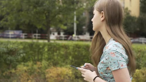 A Beautiful Young Caucasian Woman Works on a Smartphone with a Smile As She Walks Down a Street