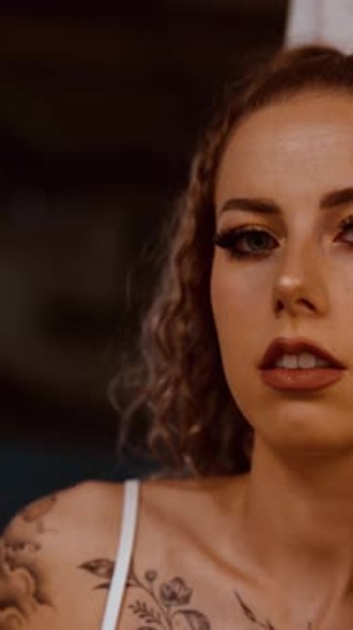 Vertical video of tattooed woman posing at warehouse pillar as fire ignites behind close up