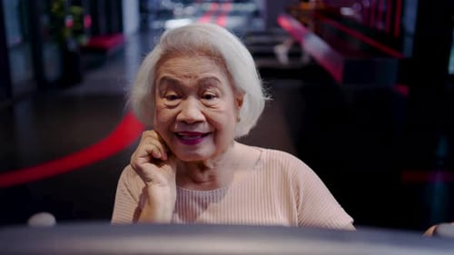 Happy elderly Asian woman with white hair exercising on a treadmill in a modern gym.