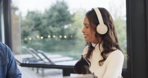 Female host answering question at studio table with headphones and mic, facing co-host