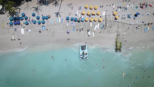 Aerial footage captures the beauty of a white sandy beach filled with lively beach umbrellas, and pe