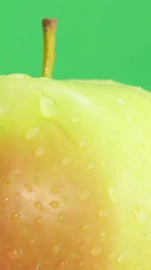 A Ripe Apple in a Raindrop Rotates on a Green Background Vertical Video