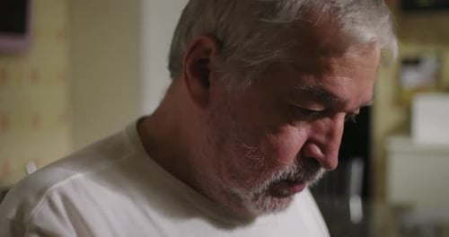 Close-up of an elderly man with dementia or age-related illness in a kitchen, looking down in