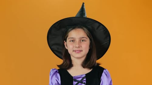 Smiling Child in Witch Costume on Orange Background
