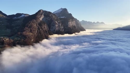 Cinematic aerial footage of alpine mountains emerging above a dense sea of clouds at sunrise,