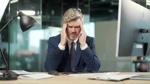 Exhausted, overworked mature office worker sitting in workplace with a severe headache massaging