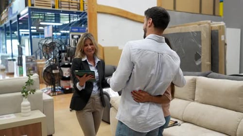 Professional Saleswoman Assisting Young Couple in Furniture Store