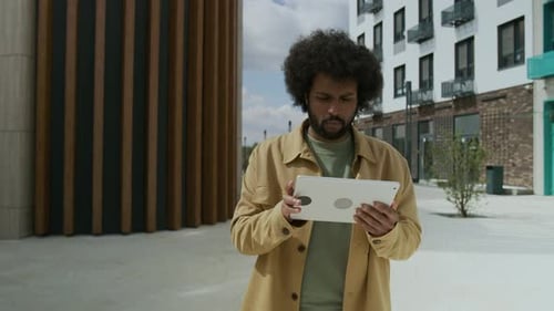 Biracial Mann im gelben Hemd arbeitet sorgfältig an Projekt auf seinem Tablet