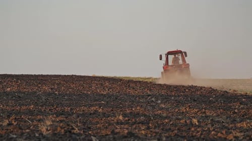 Brown field background and a tractor plowing the soil