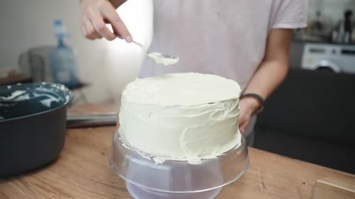 Eine Frau streut mit einem Löffel eine Schicht weißer Sahne auf den Kuchen, die Kamera zoomt langsam heran.