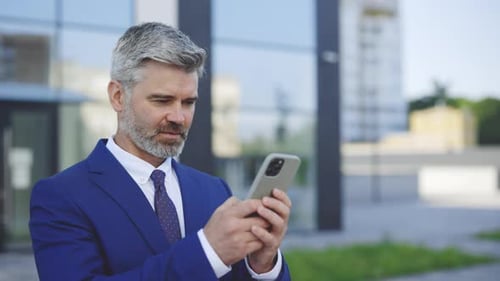 Successful Businessman Texting Messages On Modern Smartphone Standing In Business District Having