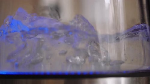 Water boiling inside of a illuminated bottle, shallow focus close-up, slowmo