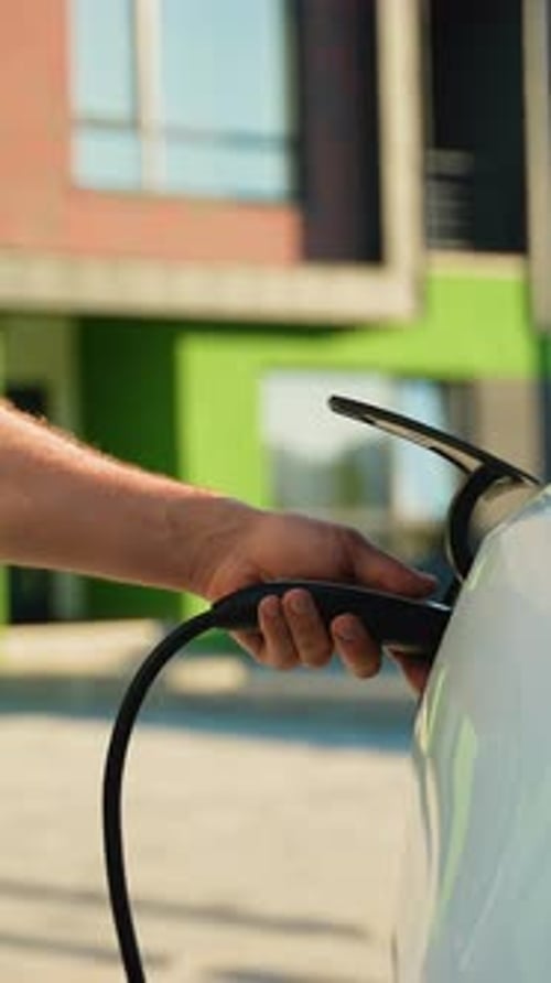Man charging electric car in suburban environment
