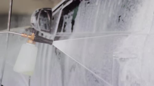 Close-up of car wash foam gun spraying white foam on car window