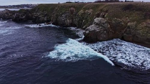 Waves crash against rocky shore during cloudy day by the coast