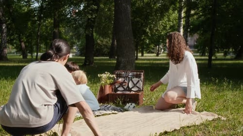 Parents Setting Up Food on Blanket for Picnic in Park, Children Playing with Dog