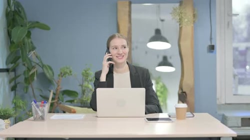 Smiling Woman Talking on Phone at Modern Desk
