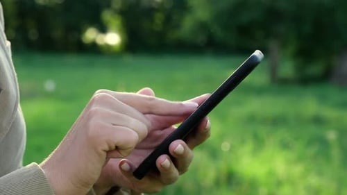 Nahaufnahme weiblicher Hände mit einem Smartphone, Naturhintergrund, Frau mit Handy im Sonnenuntergang