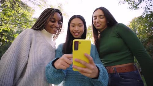 Three Young Women Using Phone While Having Fun in the Park and Laughing Social Media App