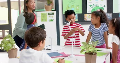 In school, teacher and students discussing science project with wind turbines