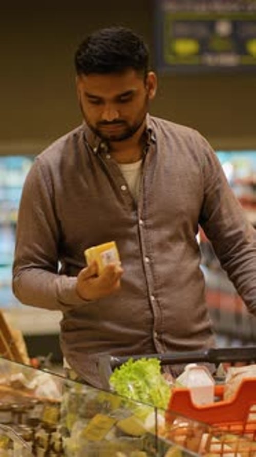 Young Man Choosing Cheese at the Supermarket Grocery Store