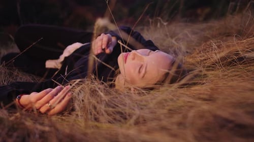 A Young Beautiful Girl Lies in a Field on Dry Grass and Looks at the Camera