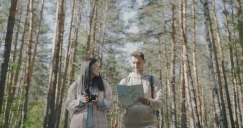 Young Man and Woman Walking in Forest and Looking at Map Exploring Area on Summer Day
