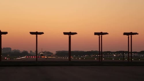 Airplane taking off at dusk with runway lights and city silhouette in the background, warm sky