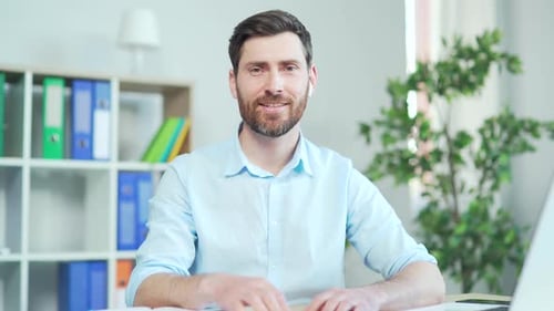 Man in Blue Shirt at Desk Looking at Camera
