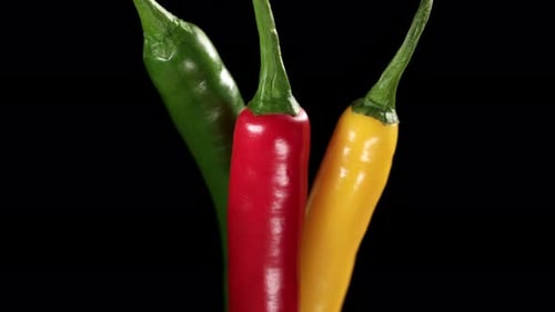 Close-up pedestal shot of green, red, and yellow chili peppers on black background