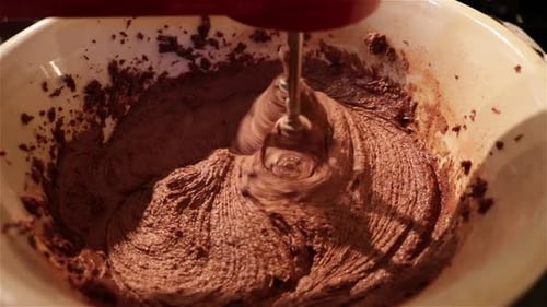 Close up of inside of a bowl while two hand mixer blades spin through smooth batter