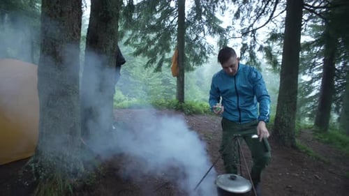 A Guy Cooks Food in a Cauldron on a Fire on a Camping Trip with a Tent