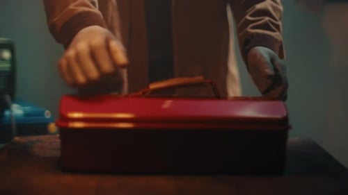 Mechanic Placing Red Metal Toolbox on Work Surface in Dim Workshop Environment