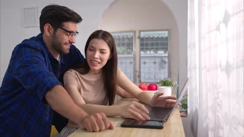 Smiling Couple Works Together at Home on Laptop