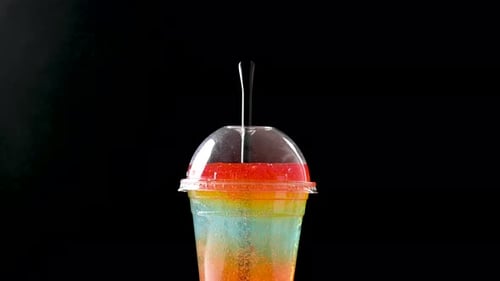 Colorful slushie spinning in clear plastic cup on black background