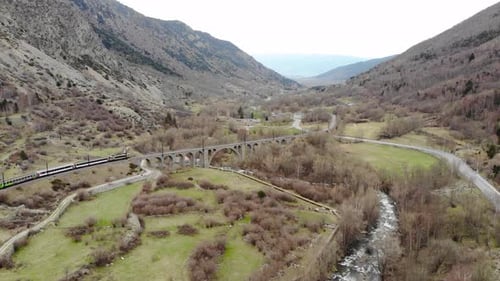Aerial: passenger train in a valley crossing a river on ancient viaduct in the Pyrenees, southern Fr
