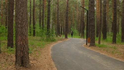 Brunette Woman in Tight Black Cardio Wear Runs Through Forest Park Heart Pumping During Intense