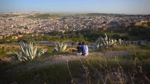 Adventurous couple of man and woman sit on dry hillside overlooking Fez Morocco