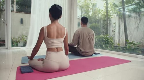 Vista trasera del hombre y la mujer sentados en postura de loto mientras hacen yoga