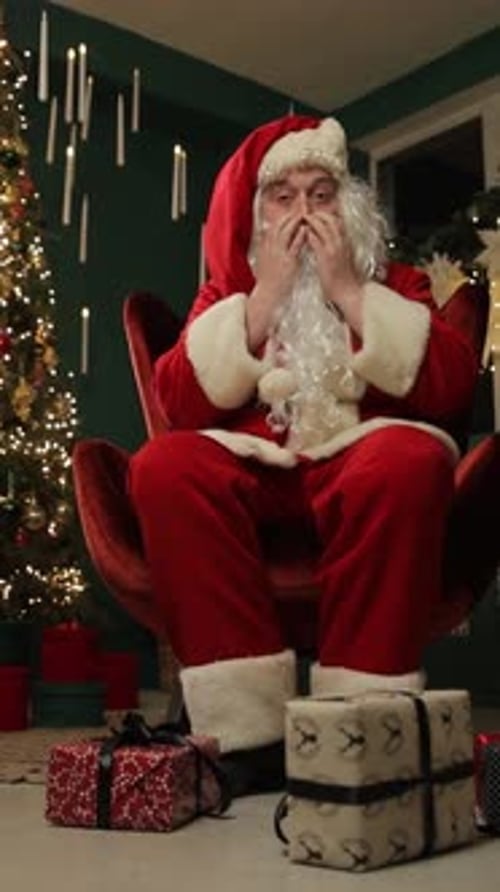 Man in Santa suit sitting by Christmas tree