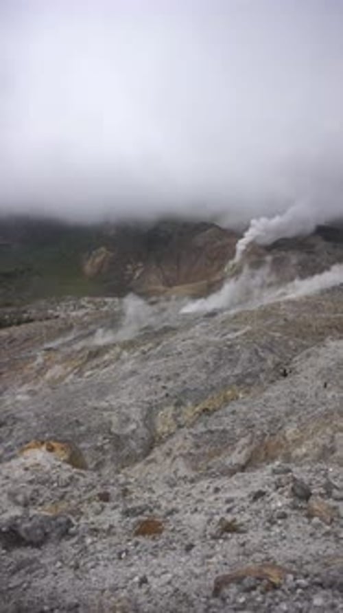 Dramatic view of Mount Papandayan crater with steaming sulfur vents under cloudy sky in Garut
