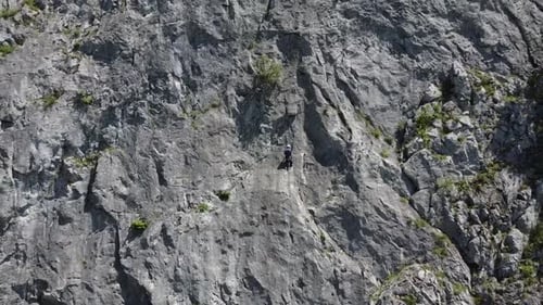 Climber hanging onto a mountain as camera pulls out wide